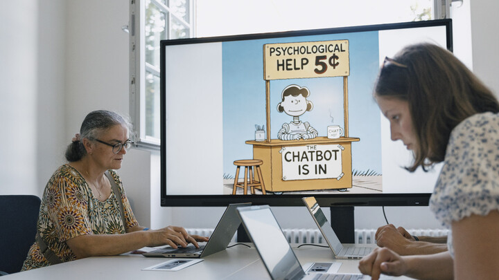 Zwei Frauen arbeiten an Laptops. Im Hintergrund zeigt ein Bilschirm eine Folie zum Thema Chatbot.