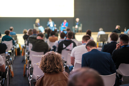 Publikum vor einer Bühne, auf der eine Podiumsdiskussion stattfindet