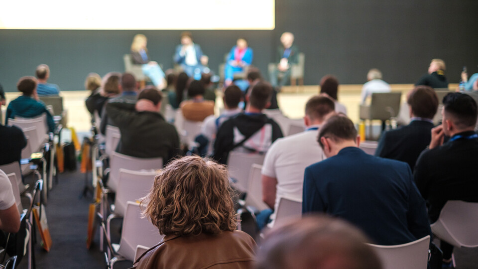 Publikum vor einer Bühne, auf der eine Podiumsdiskussion stattfindet