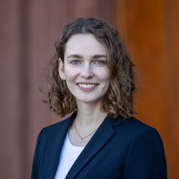 Carolin Unterricker hat braune, schulterlange Haare und trägt einen blauen Blazer. Sie lächelt in die Kamera.