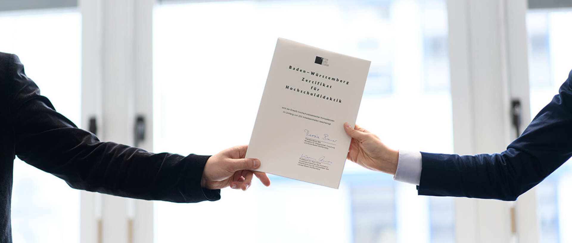 Two arms hold up a certificate for university teaching from the left and right.