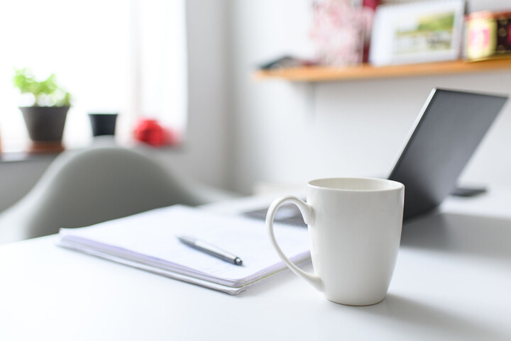 Ein Schreibblock, ein aufgeklapptes Laptop und eine Kaffeetasse.