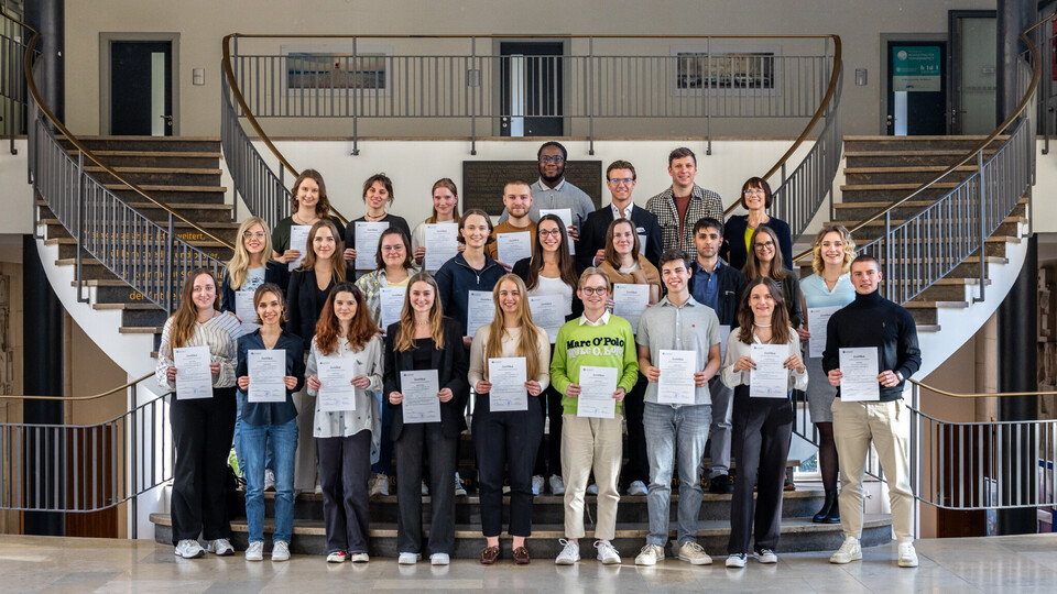 Die Absolventinnen und Absolventen des Studium Oecologicum stehen auf einer Treppe und präsentieren ihre Zertifikate