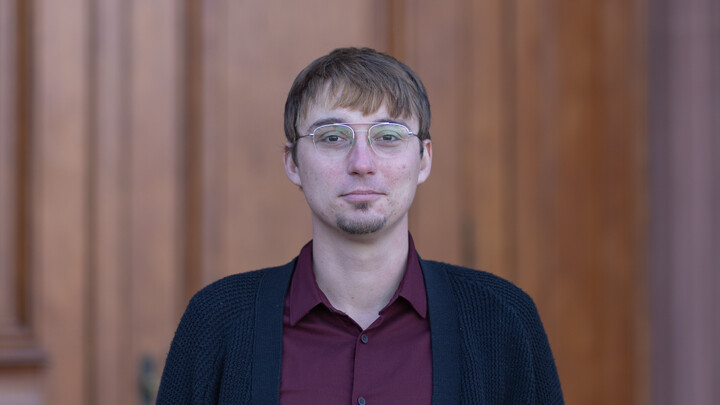 Vladislav Kucher. He is wearing a black jacket over a red shirt and is standing in front of one of the castle doors.