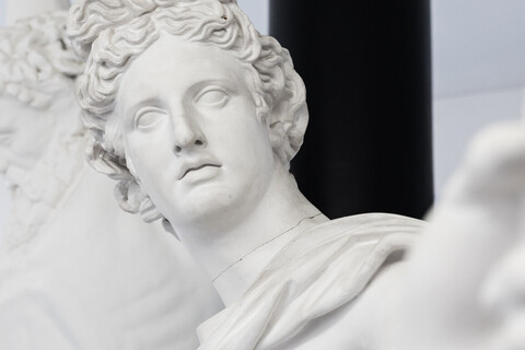 Eine Skulptur streckt den Linken Arm zur Kamera aus. Im Hintergrund steht eine nackte Männerskulptur, die ihre Arme über dem Kopf ausgestreckt hält.