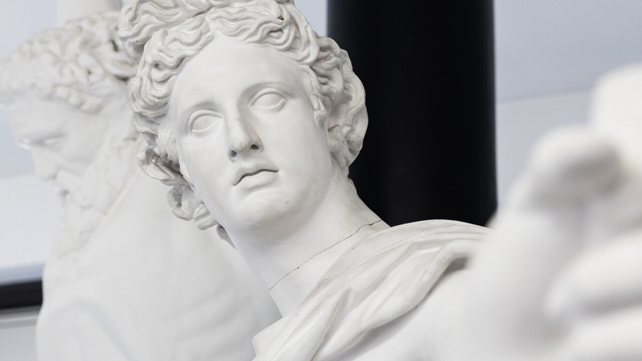 Eine Skulptur streckt den Linken Arm zur Kamera aus. Im Hintergrund steht eine nackte Männerskulptur, die ihre Arme über dem Kopf ausgestreckt hält.