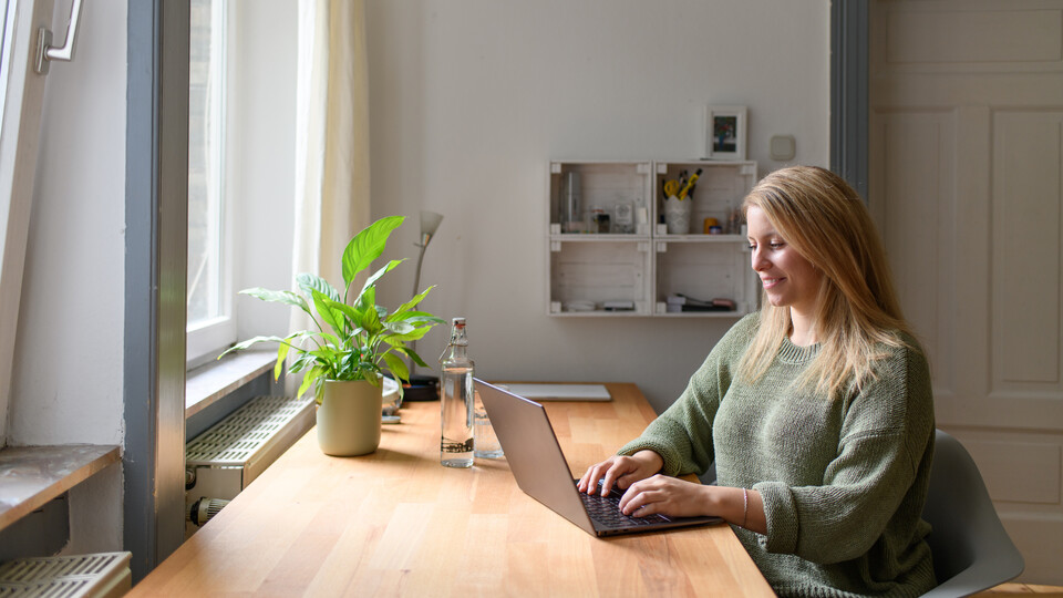 Studierende sitzt am Tisch und arbeitet am Laptop