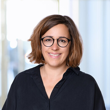 Nina Gropper hat kurze braune Haare. Sie trägt eine schwarz umrandete Brille und eine schwarze Bluse.