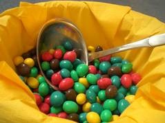 Eine mit gelben Servietten ausgekleidete Schüssel, in der sich eine Schöpfkelle und viele bunt überzogene Bonbons befinden.