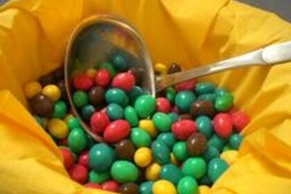 Eine mit gelben Servietten ausgekleidete Schüssel, in der sich eine Schöpfkelle und viele bunt überzogene Bonbons befinden.