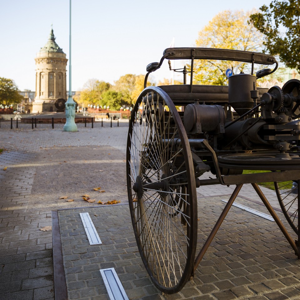 Denkmal für Carl Benz in Mannheim: Nachbau des Benz-Patent-Motorwagen. Im Hintergrund der Wasserturm.