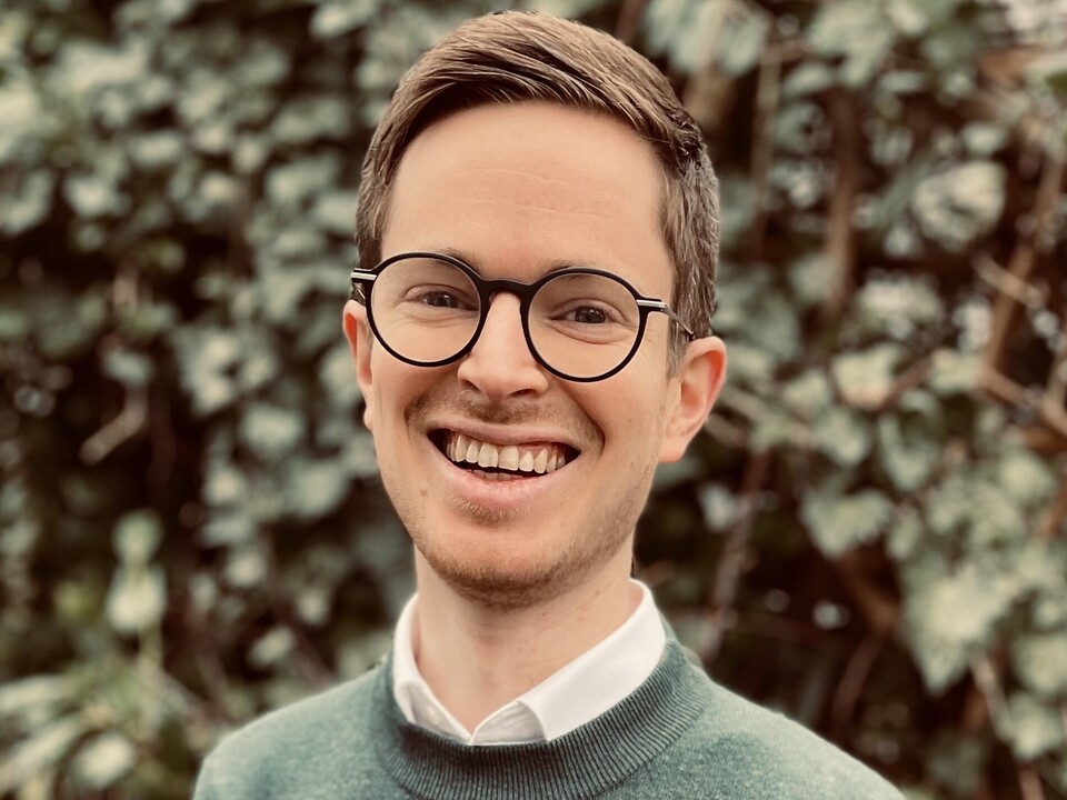 Florian Pethig. He is wearing a green sweater and is standing in front of a green hedge.