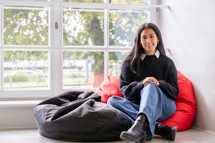 Studentin sitzt auf einem Sitzkissen vor einem Fenster