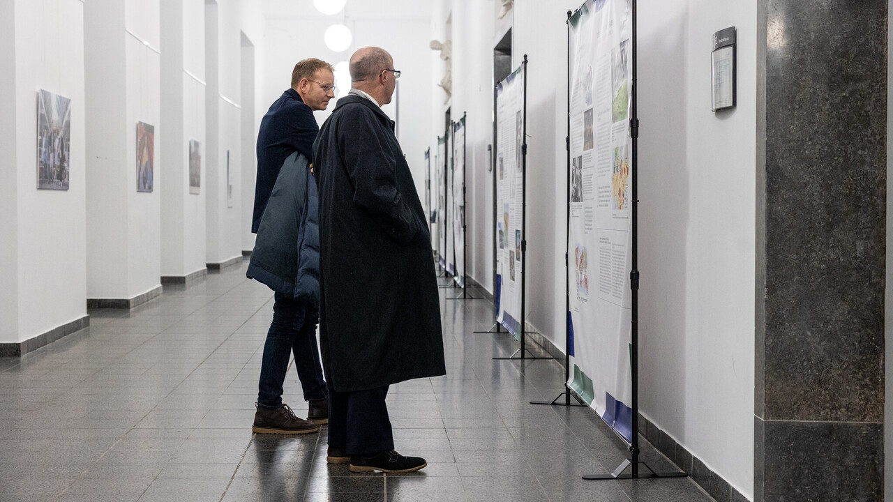 Zwei Personen stehen vor mehreren Austellungstafeln bei einer Vernissage