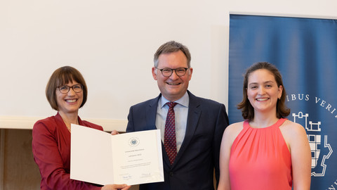 Drei Personen in schicker Kleidung stehen nebeneinander auf einer Bühne. Die Person links hält eine Urkunde über einen Lehrpreis der Uni Mannheim an Philipp Gassert in der Hand.