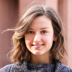 Tsvetina Yancheva hat braunes, fast schulterlanges welliges Haar. Sie hat braune Augen und lächelt. Sie trägt kleine Ohrringe und einen dunkelgrauen Strickpullover.