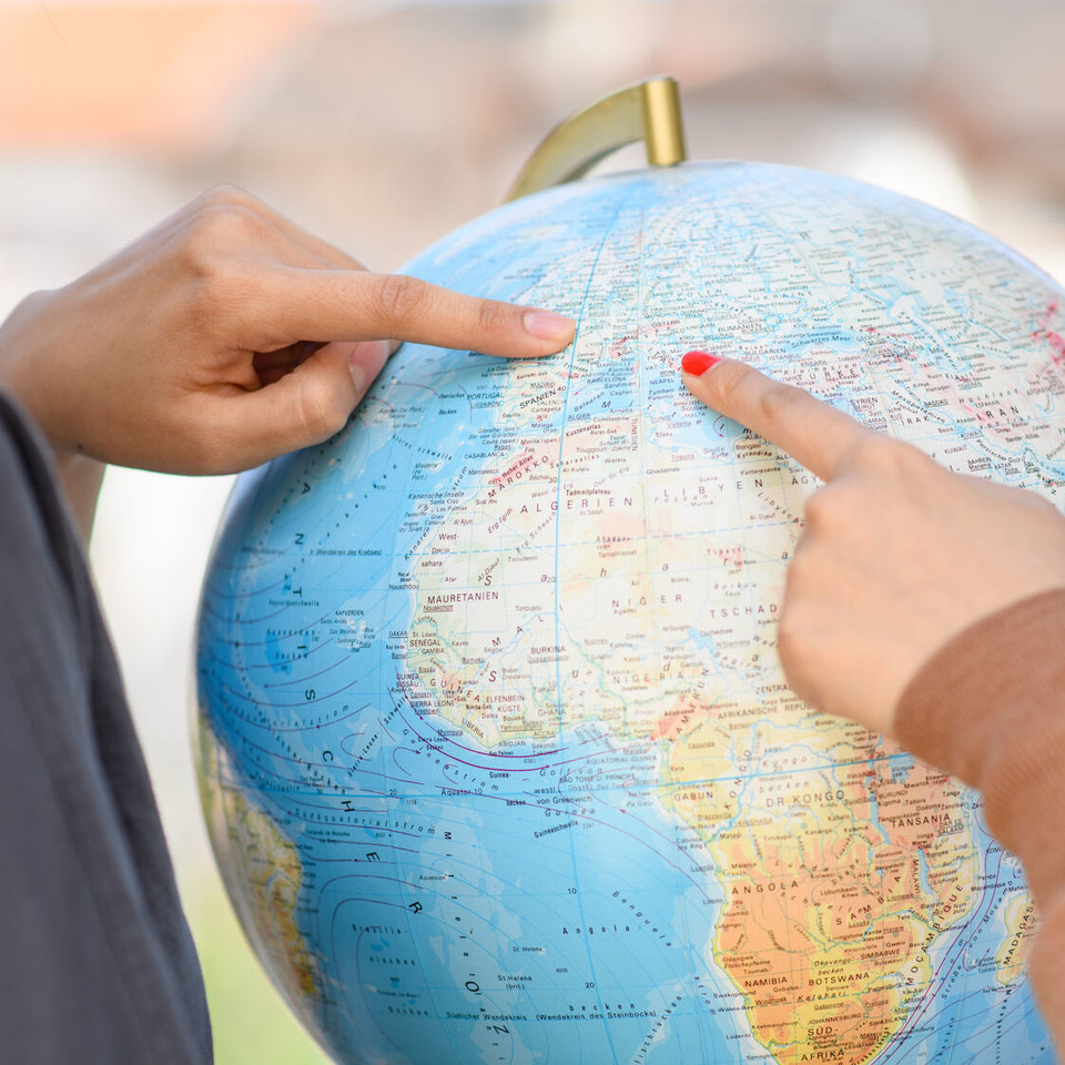 Zwei Personen zeigen mit dem Finger auf einen Globus