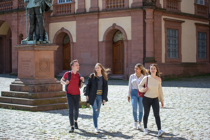Vier Studierende laufen auf dem Ehrenhof und unterhalten sich miteinander.