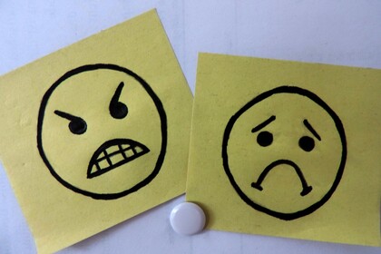 Zwei gelbe Post-Its wurden an eine weiße Wand gepinnt. Auf den einen ist ein wütender Emoji, auf den anderen ein trauriger Smiley gezeichnet.
