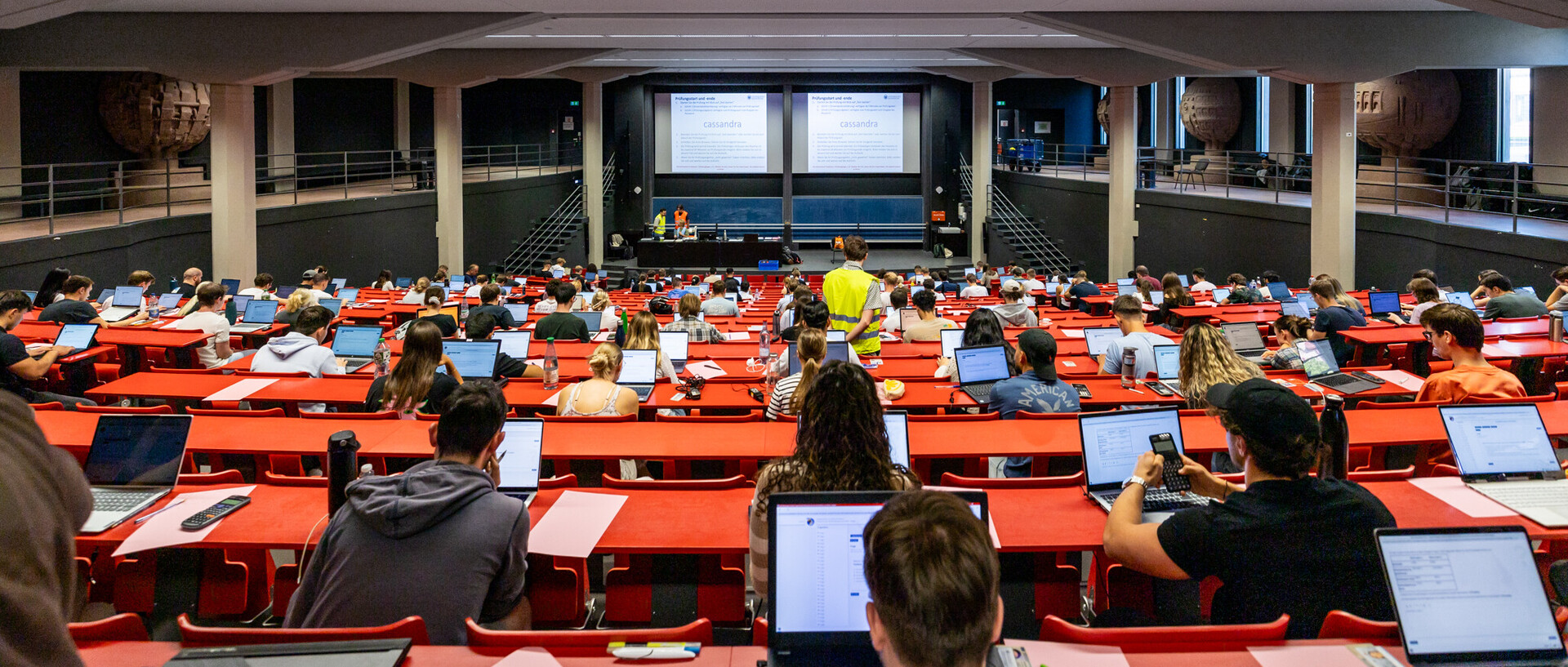 Blick von hinten in einen Hörsaal während einer digitalen Prüfung: Studierende sitzen an ihren eigenen Laptops, konzentriert und mit Abstand verteilt – moderne Prüfungsform im Einsatz