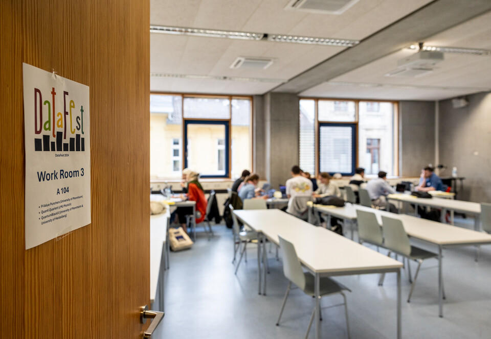 Blick in einen SEminarraum, in dem Studierende konzentriert an Laptops arbeiten. An der Tür hängt das DataFest-Logo