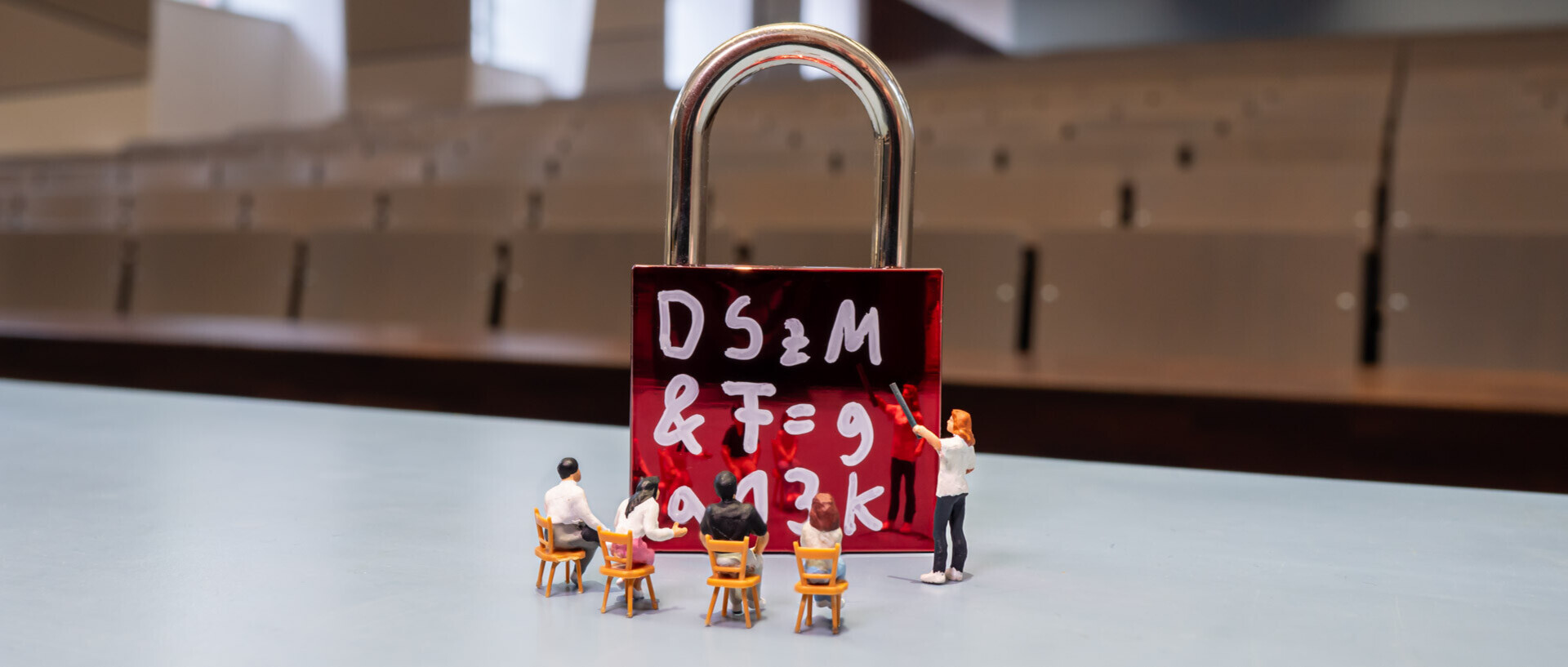 The photo shows participants at a training course. All of the figures are miniature figures sitting in front of a curtain wall that serves as a blackboard for the miniature teacher.