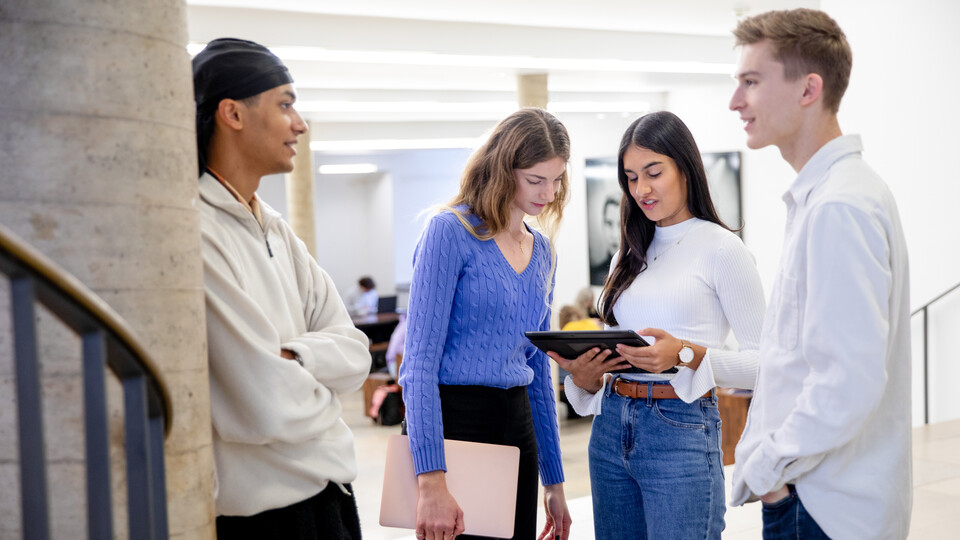 Vier Studierende im Gespräch, eine zeigt den anderen etwas auf einem Tablet.