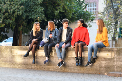 Fünf Studierende sitzen auf einer Mauer und unterhalten sich.