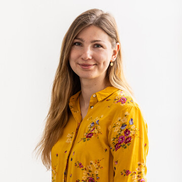Lea Gorski hat blonde, lange Haare und trägt eine gelbe Bluse. 