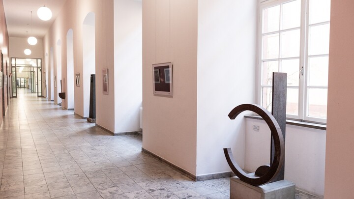 In einem Flur steht vor einem Fenster eine geometrische Plastik aus Metall.