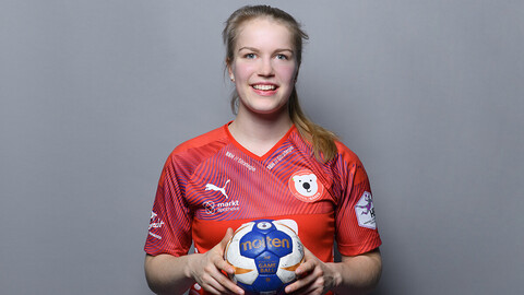 Amelie Möllmann trägt ein rotes Trikot und hält einen Handball in den Händen.