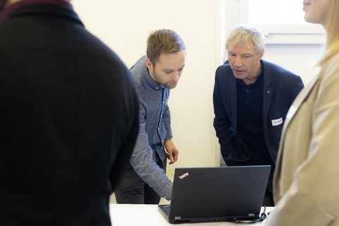 Zwei Männer schauen interessiert auf einen Laptop, der vor ihnen auf einem Tisch steht.