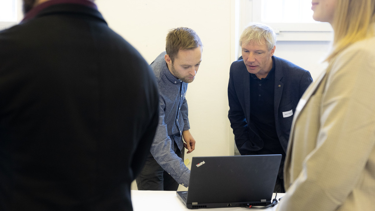 Zwei Männer schauen interessiert auf einen Laptop, der vor ihnen auf einem Tisch steht.