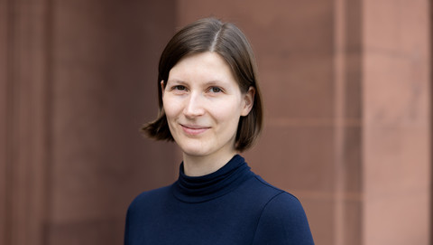 Jana Kuhlemann. She is wearing a black sweater and is standing in front of a brown stonewall.