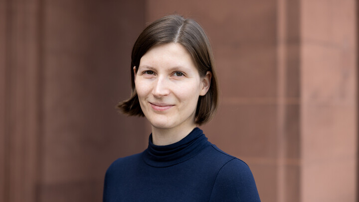 Jana Kuhlemann. She is wearing a black sweater and is standing in front of a brown stonewall.