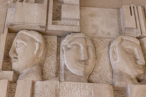 In einer Steinmauer sind drei Gesichter eingemeißelt.