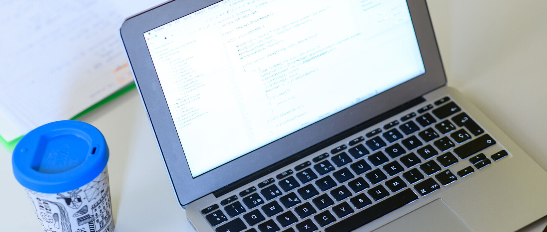 aufgeklappter Laptop, daneben liegt ein Smartphone und ein to go Becher steht daneben.
