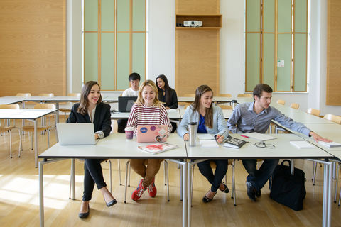 Sechs Studierende arbeiten in einem Seminarraum. Vor ihnen liegen Laptops, Notizblöcke und Bücher.