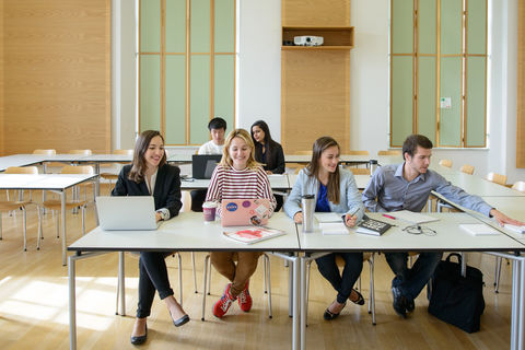 Sechs Studierende arbeiten in einem Seminarraum. Vor ihnen liegen Laptops, Notizblöcke und Bücher.