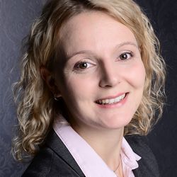Kerstin Lux hat mittelange blonde Haare. Sie trägt ein rosanes Oberteil und einen dunklen Blazer darüber.
