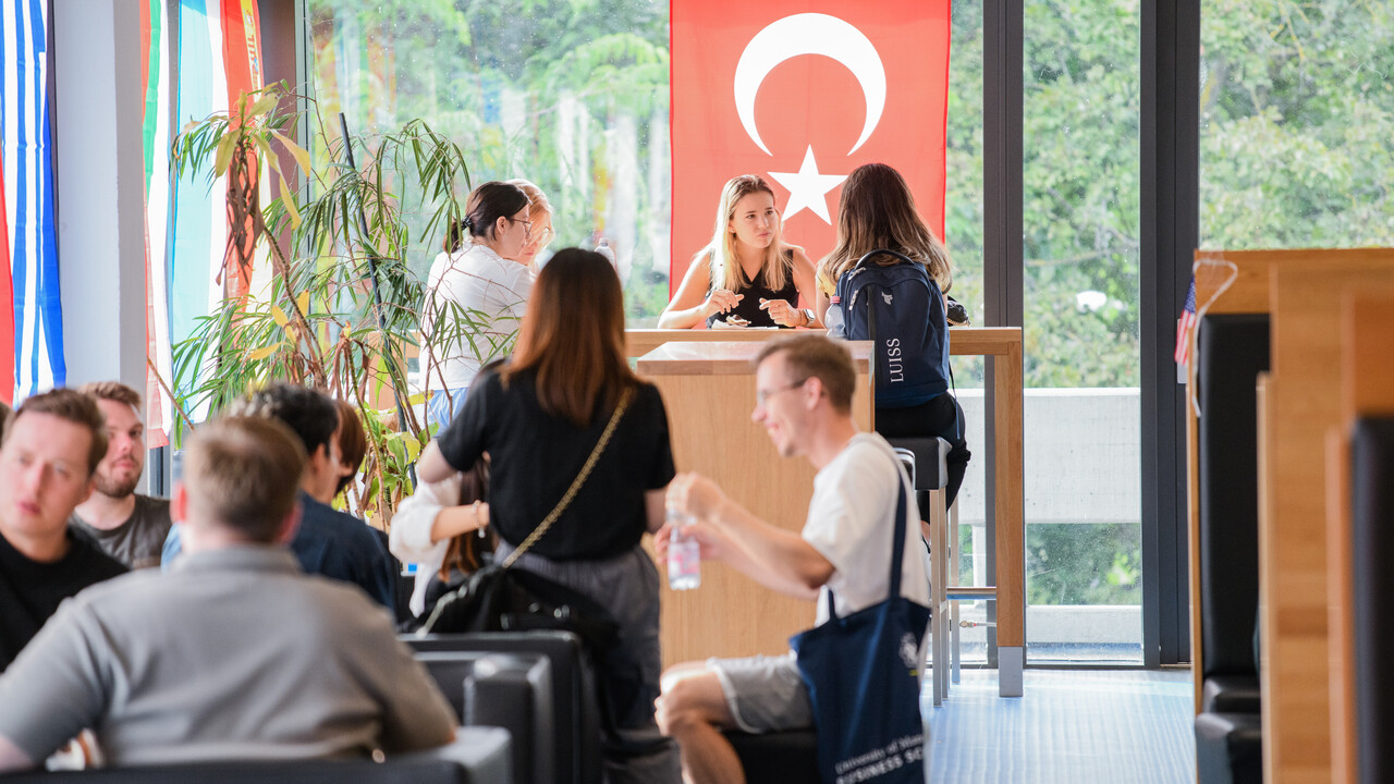 Studierende in der Mensa unterhalten sich, im Hintergrund ist groß die türkische Landesflagge zu sehen.