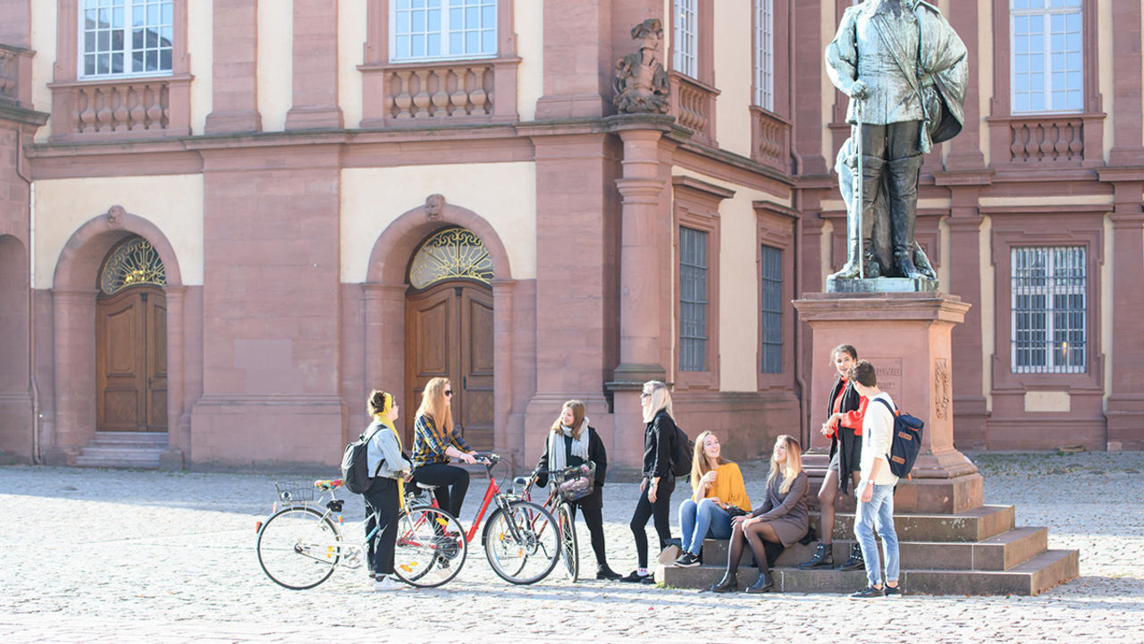 Eine Gruppe von Studierenden mit und ohne Fahrrad steht rund um das Karl-Ludwig-Denkmal auf dem Ehrenhof