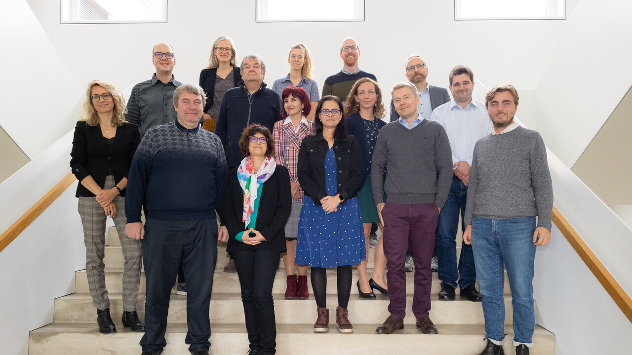 Viele Personen in schicker Kleidung stehen nebeneinander auf einer Treppe in einem Gebäude.