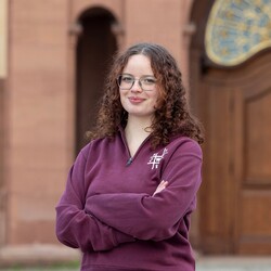 Felice is wearing a claret pullover with "VWL" written on it. She has glasses and curly brown hair.