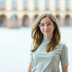 Eine junge Frau mit langen, dunkelblonden Haaren und einer transparenten Brille lächelt. Sie trägt ein helles Rollkragenshirt.