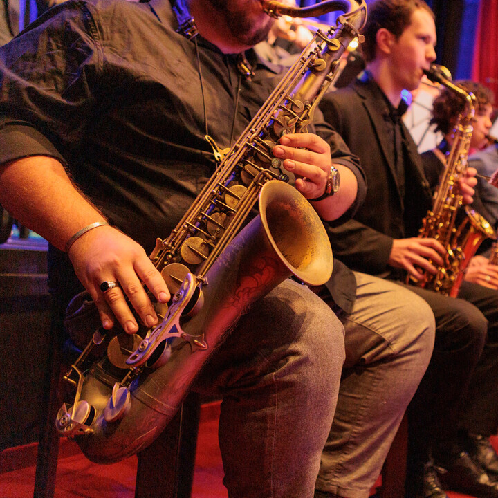 Vier Saxofonisten sitzen nebeneinander, im Fokus des Bildes ist das Instrument eines Spielers.
