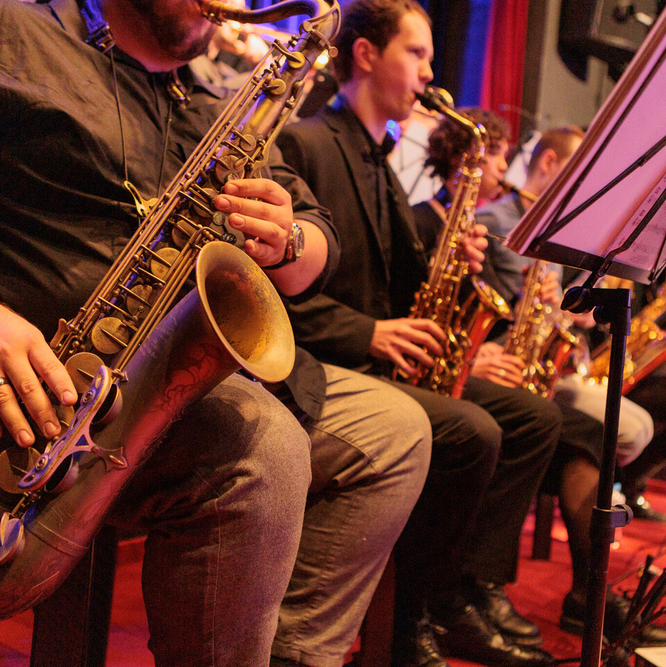 Vier Saxofonisten sitzen nebeneinander, im Fokus des Bildes ist das Instrument eines Spielers.