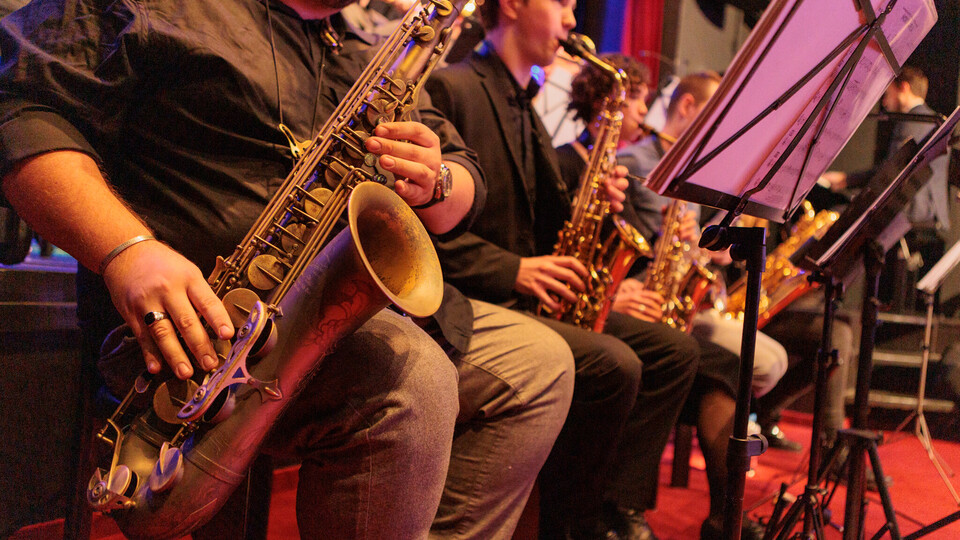 Vier Saxofonisten sitzen nebeneinander, im Fokus des Bildes ist das Instrument eines Spielers.