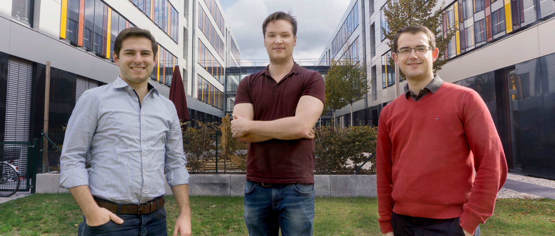 Drei Personen aus dem Team von Covexo stehen auf einer Grünfläche zwischen zwei Gebäuden.