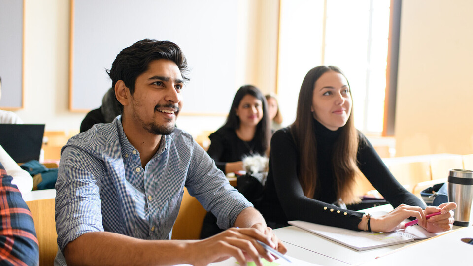 Lehrveranstaltung Eine Studentin und ein Student hören begeistert bei einem Vortrag zu.